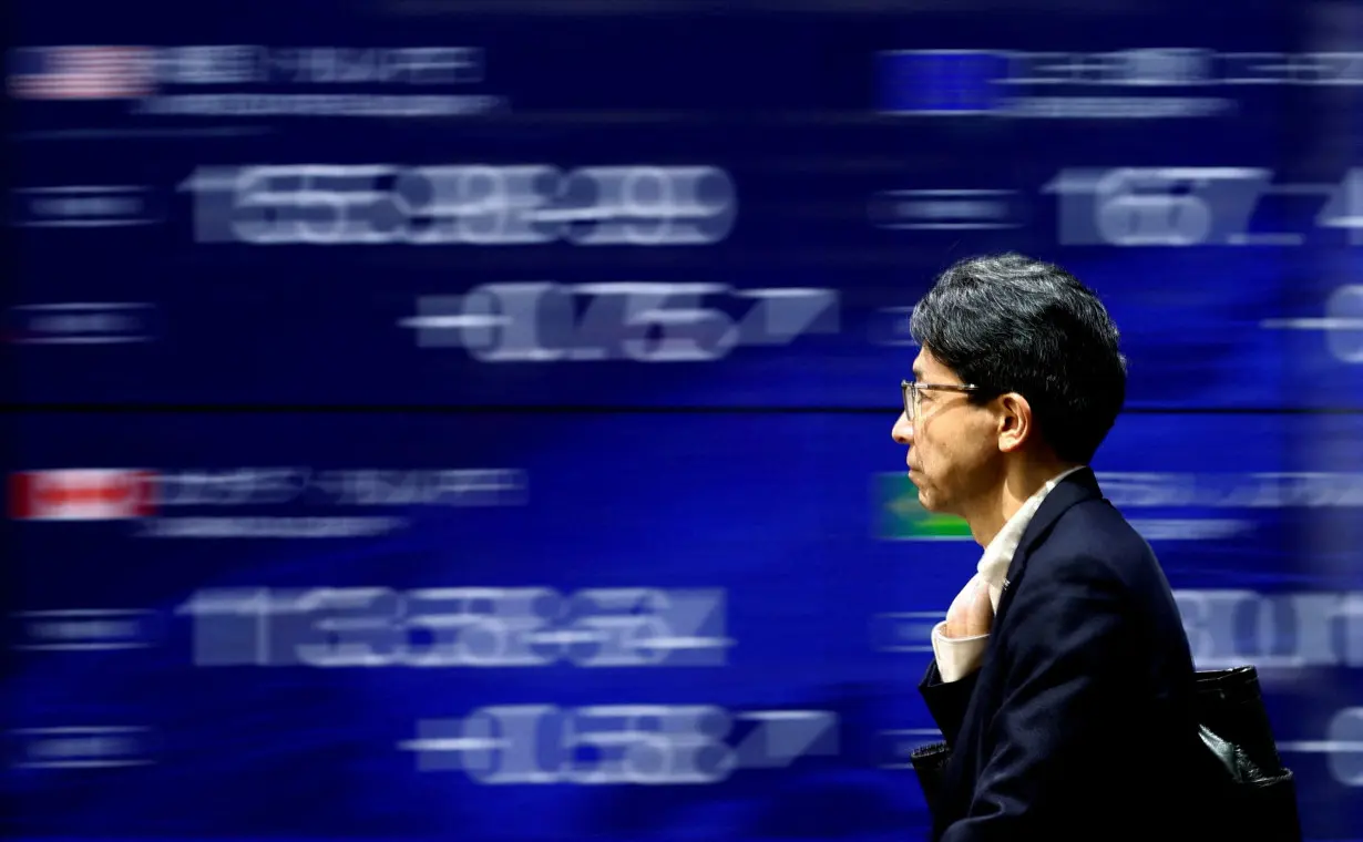 FILE PHOTO: A man walks past an electronic screen displaying the current Japanese Yen exchange rate against the U.S. dollar and other foreign currencies in Tokyo