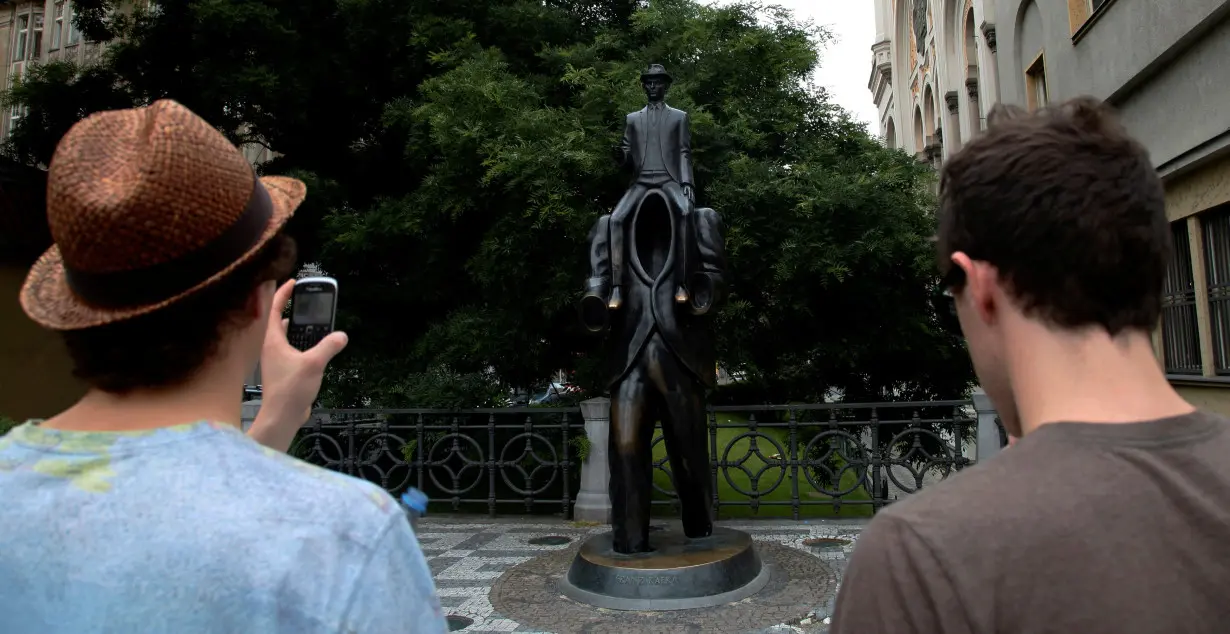 FILE PHOTO: Tourists look at a statue of famous German-language writer Franz Kafka in central Prague, on the day marking the 130th anniversary of his birth