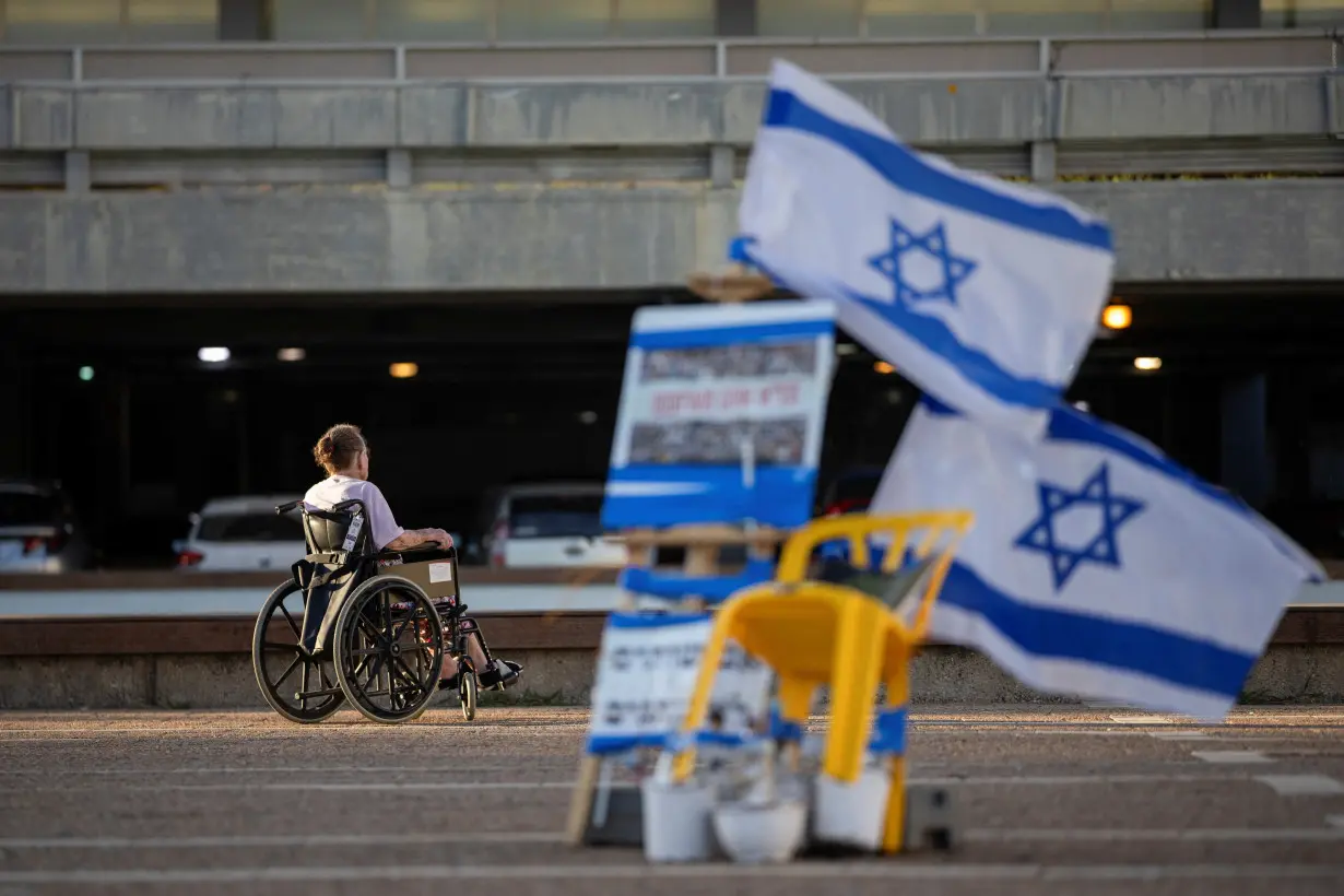 FILE PHOTO: A man in a wheelchair passes near Israeli flags and pictures of hostages kidnapped during the deadly October 7 attack by Hamas, in Tel Aviv