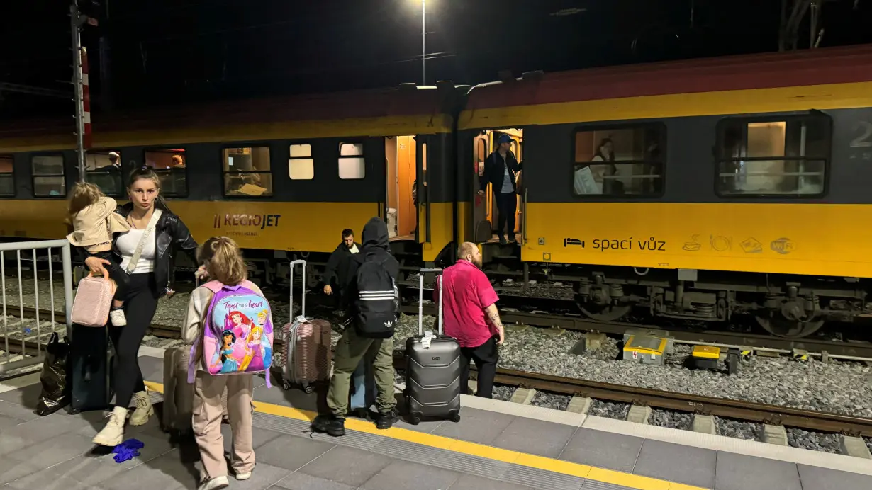 People stand near a train following a collision between a passenger train and a freight train in Pardubice