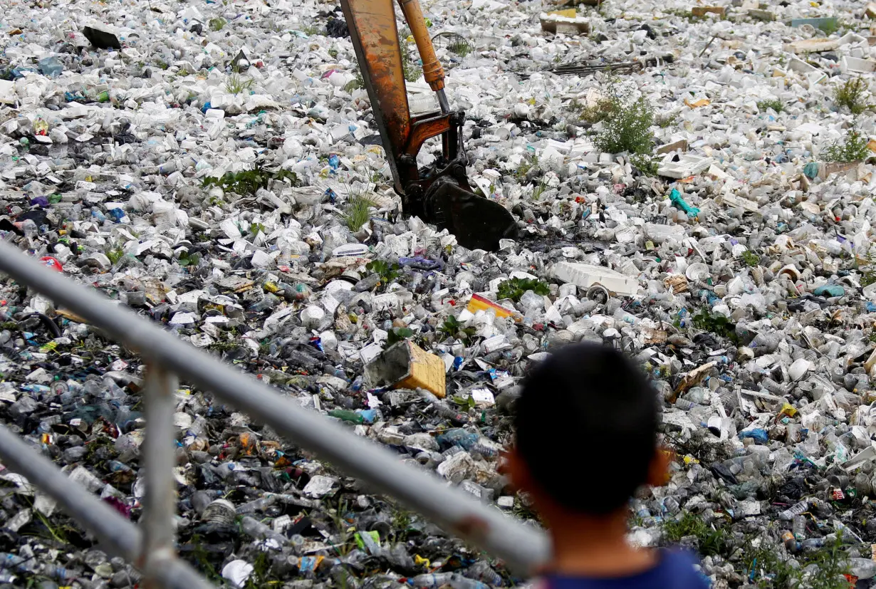 FILE PHOTO: A child watches as heavy machinery collects rubbish at a sewage canal in Phnom Penh