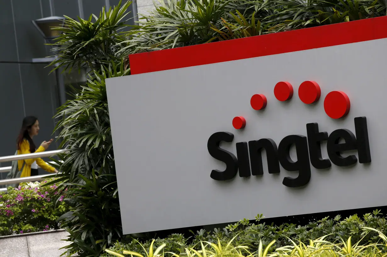 FILE PHOTO: A woman using a mobile phone walks behind a Singtel signage at their head office in Singapore