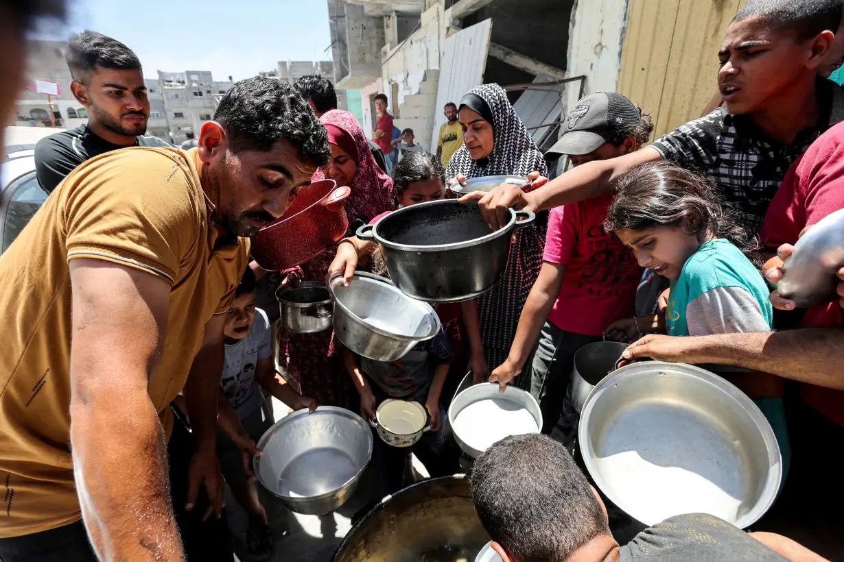 FILE PHOTO: Palestinians eat food cooked by a charity kitchen near houses destroyed in the Israeli military offensive, in Khan Younis in the southern Gaza Strip