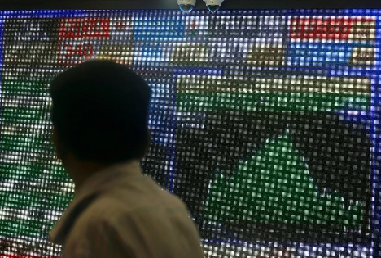 FILE PHOTO: A man looks at a screen displaying news of markets update inside the Bombay Stock Exchange (BSE) building in Mumbai