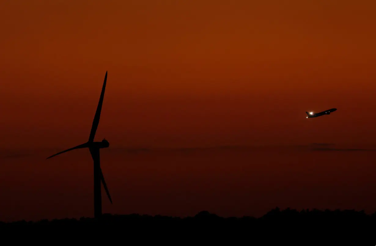A wind turbine is seen as a plane flies during sunset in Tokyo