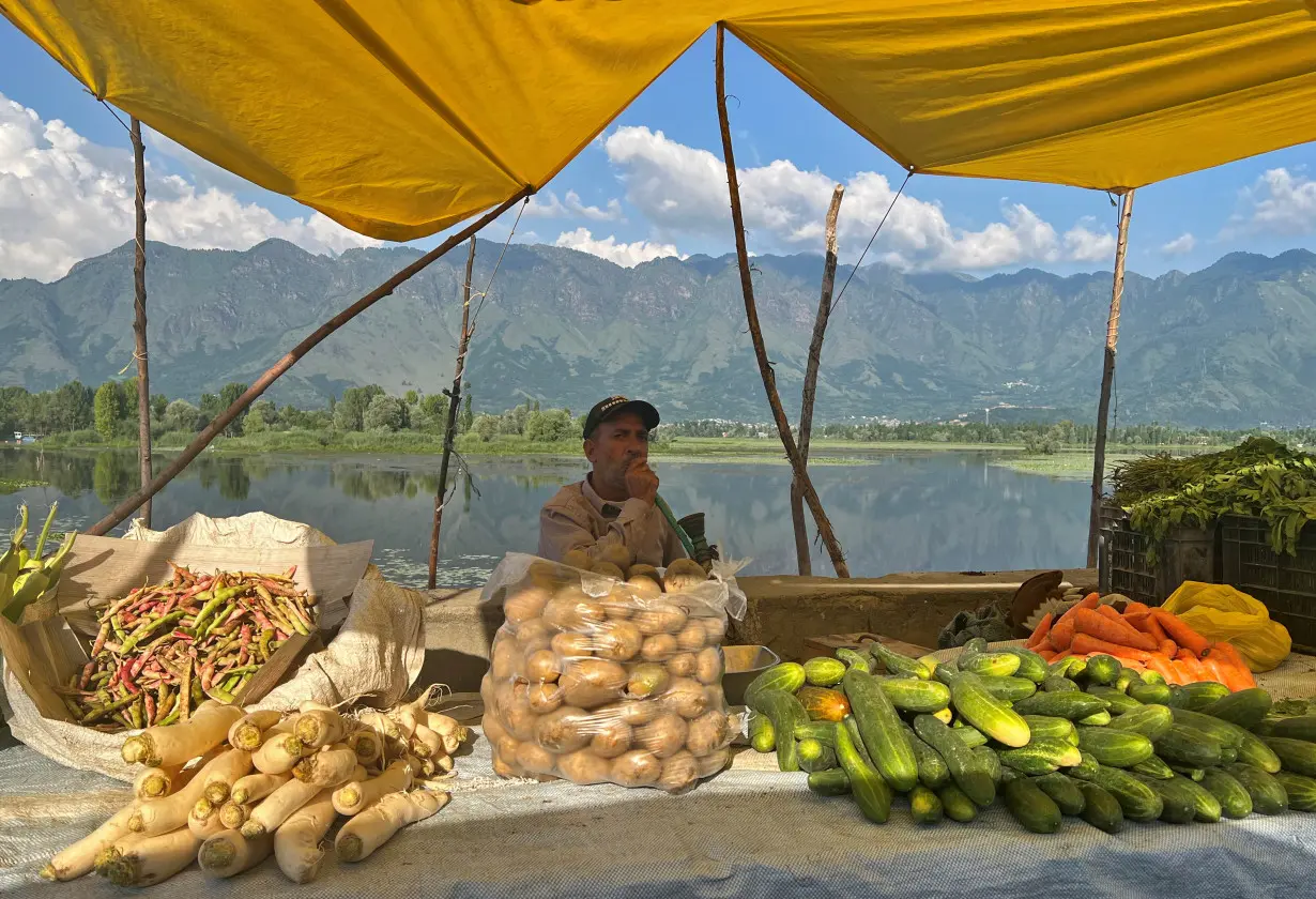 A vendor selling vegetables smokes a hookah as he waits for customers alongside a road in Srinagar