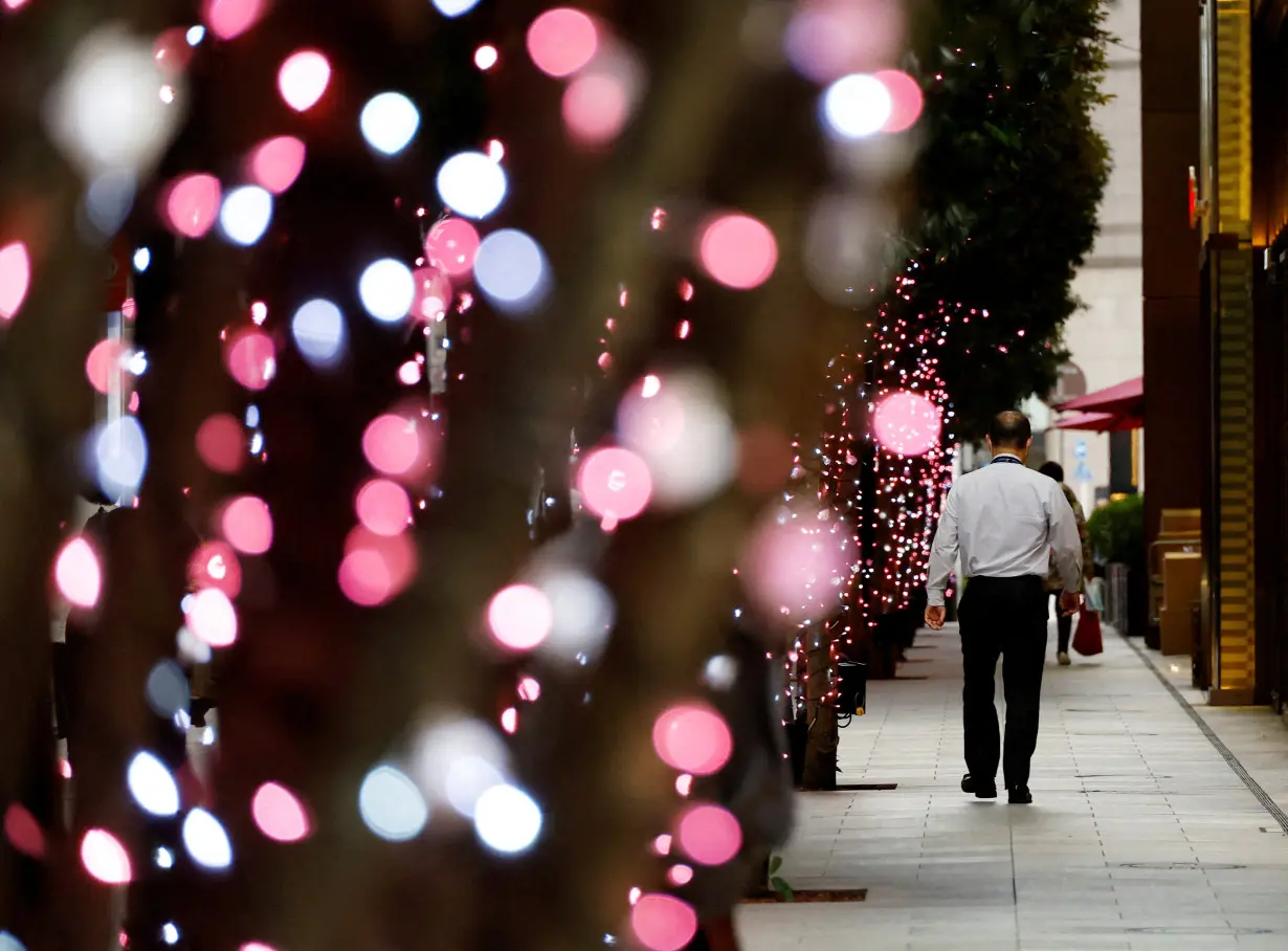 FILE PHOTO: An office worker walks past illuminated trees at a business district in Tokyo