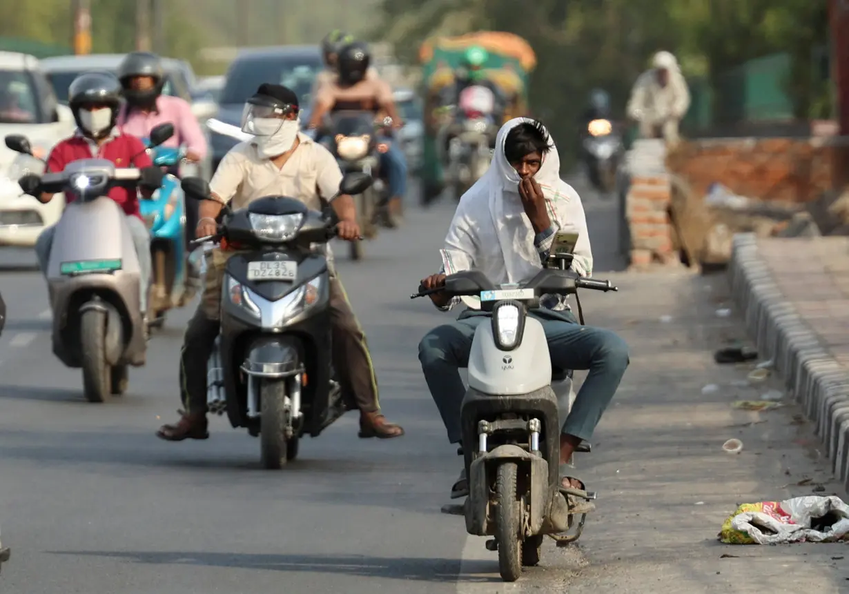 A delivery partner with Swiggy, an Indian online-delivery company, rides a low-speed two-wheeler electric vehicle on a bridge on a hot summer day, during a heatwave in New Delhi