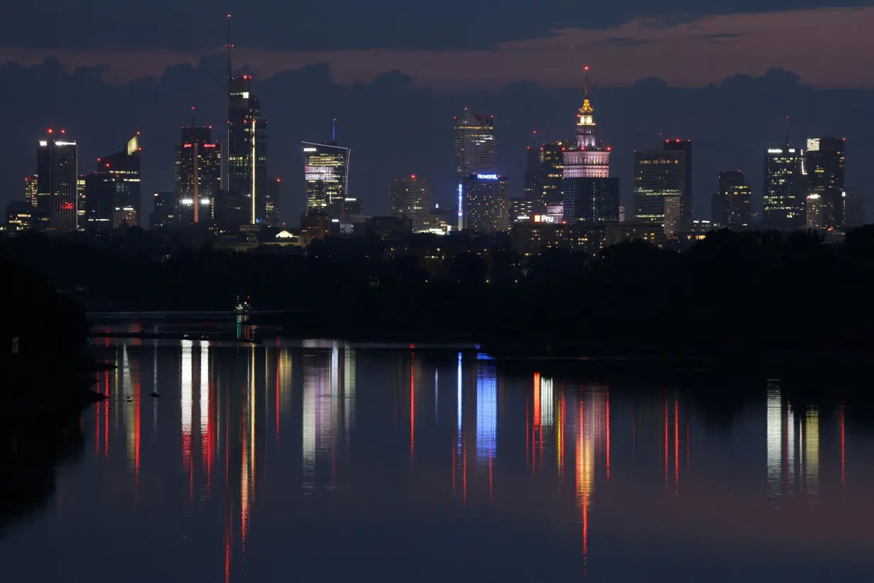 A skyline of skyscrapers is reflected in the Vistula river in the evening in Warsaw