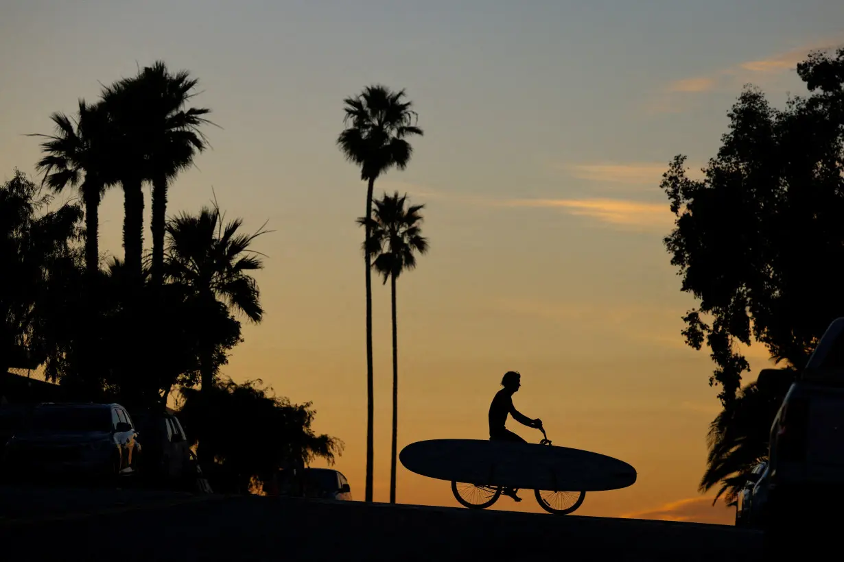 FILE PHOTO: A surfer rides his bicycle with surfboard in California