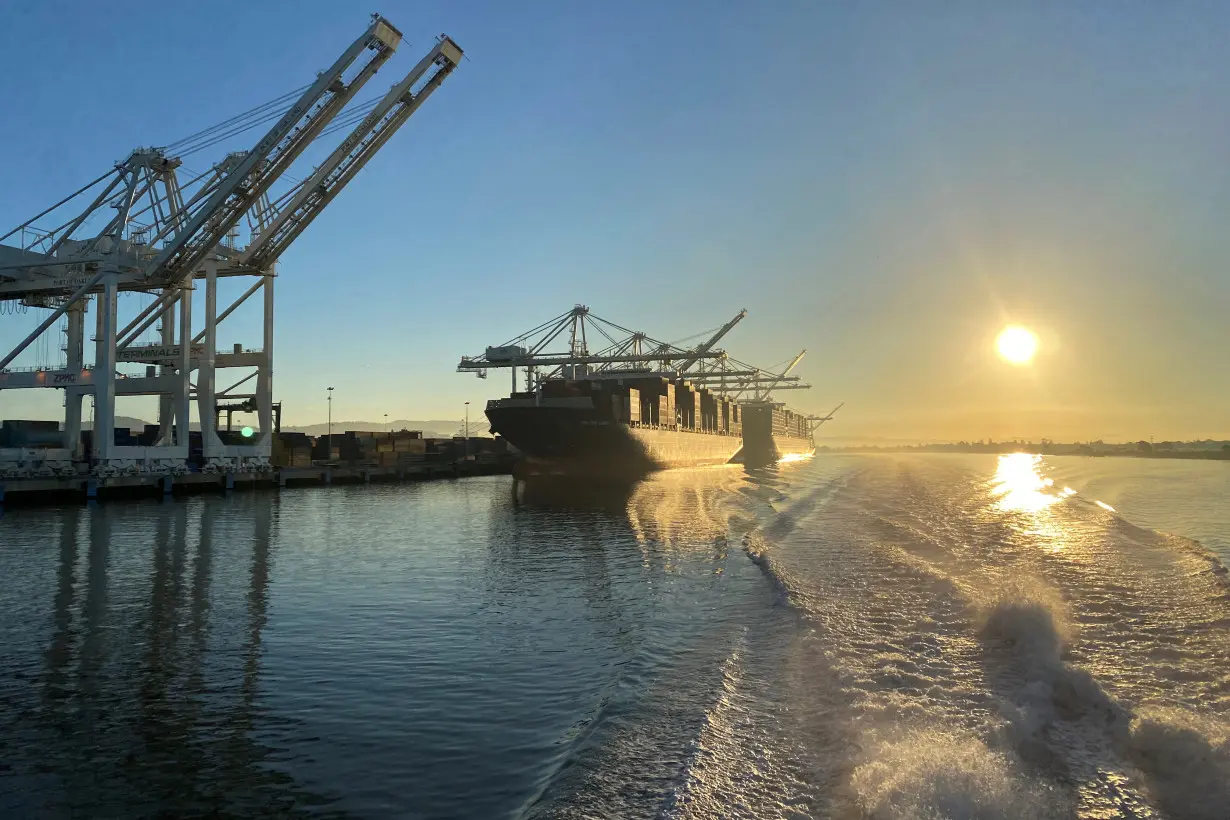 The sun rises past the cranes and a container ship at the Port of Oakland