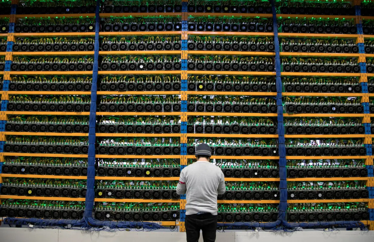 A worker checks the fans on miners at the cryptocurrency farming operation Bitfarms in Farnham, Quebec