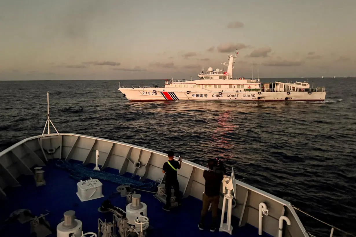 FILE PHOTO: Members of the media take footage of a Chinese Coast Guard vessel blocking a Philippine Coast Guard vessel on its way to a resupply mission at Second Thomas Shoal in the South China Sea