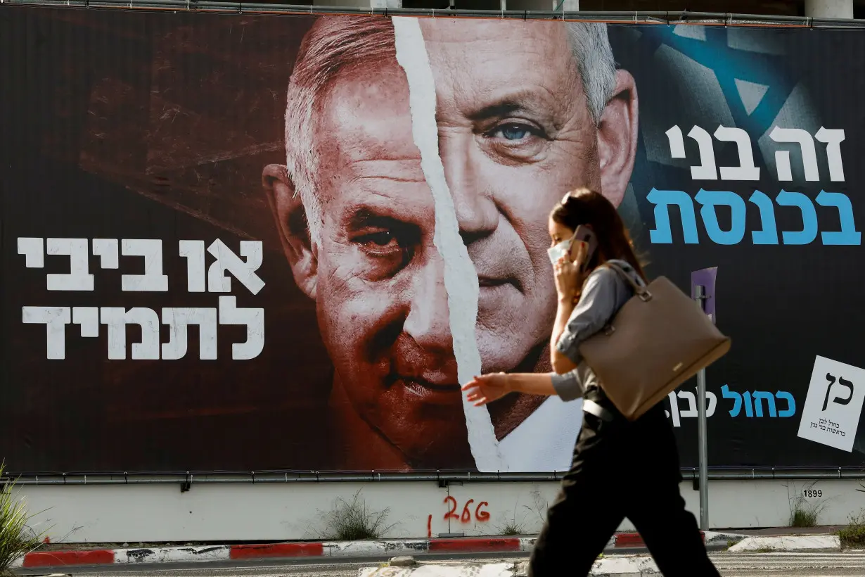 FILE PHOTO: A woman walks past a Blue and White party election campaign banner depicting its leader, Israeli Defence Minister Benny Gantz, alongside Israeli Prime Minister Benjamin Netanyahu ahead of the March 23 ballot, in Tel Aviv