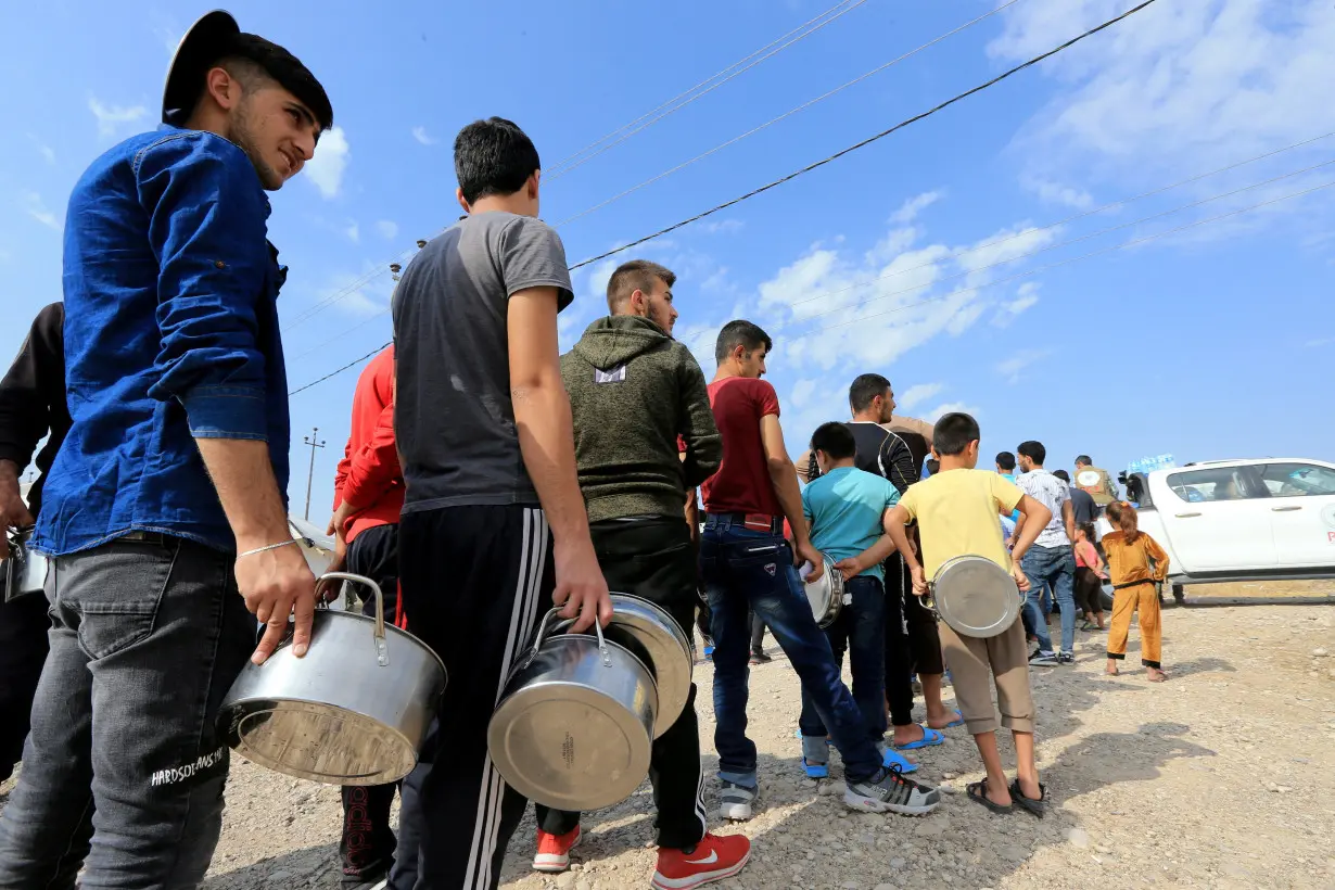 FILE PHOTO: Syrian displaced families, who fled violence after the Turkish offensive in Syria, stand in queue to get their food from Barzani charity at a refugee camp in Bardarash on the outskirts of Dohuk