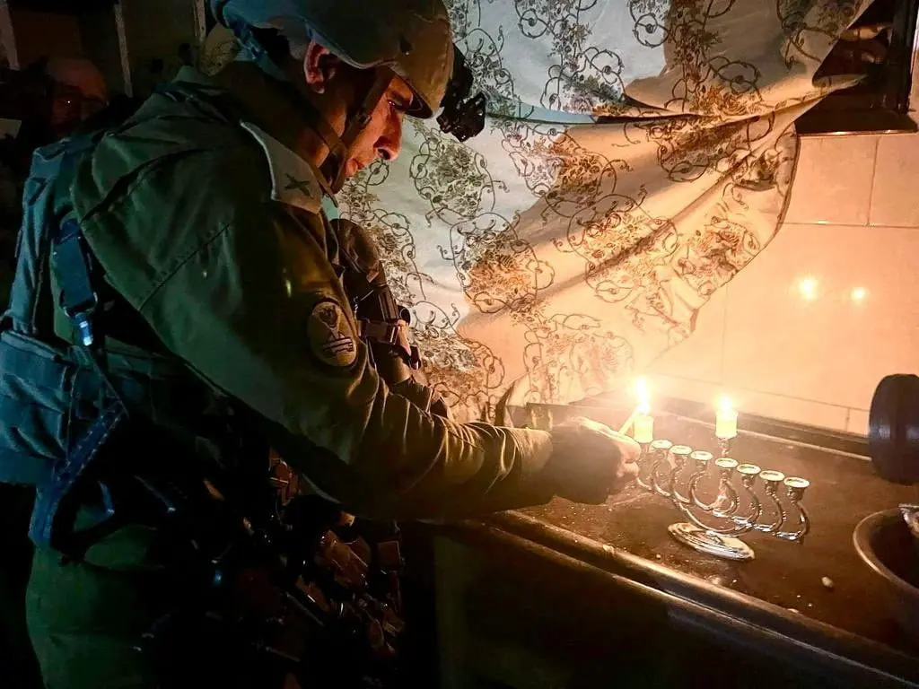 An Israeli soldier lights oil candles burning on a Hanukkiah during the Jewish holiday of Hanukkah, amid the ongoing conflict between Israel and the Palestinian Islamist group Hamas, in the Gaza Strip