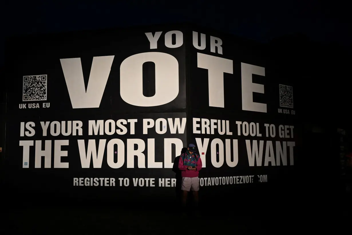 A reveller stands in front of a banner urging people to vote, at Worthy Farm in Somerset during the Glastonbury Festival