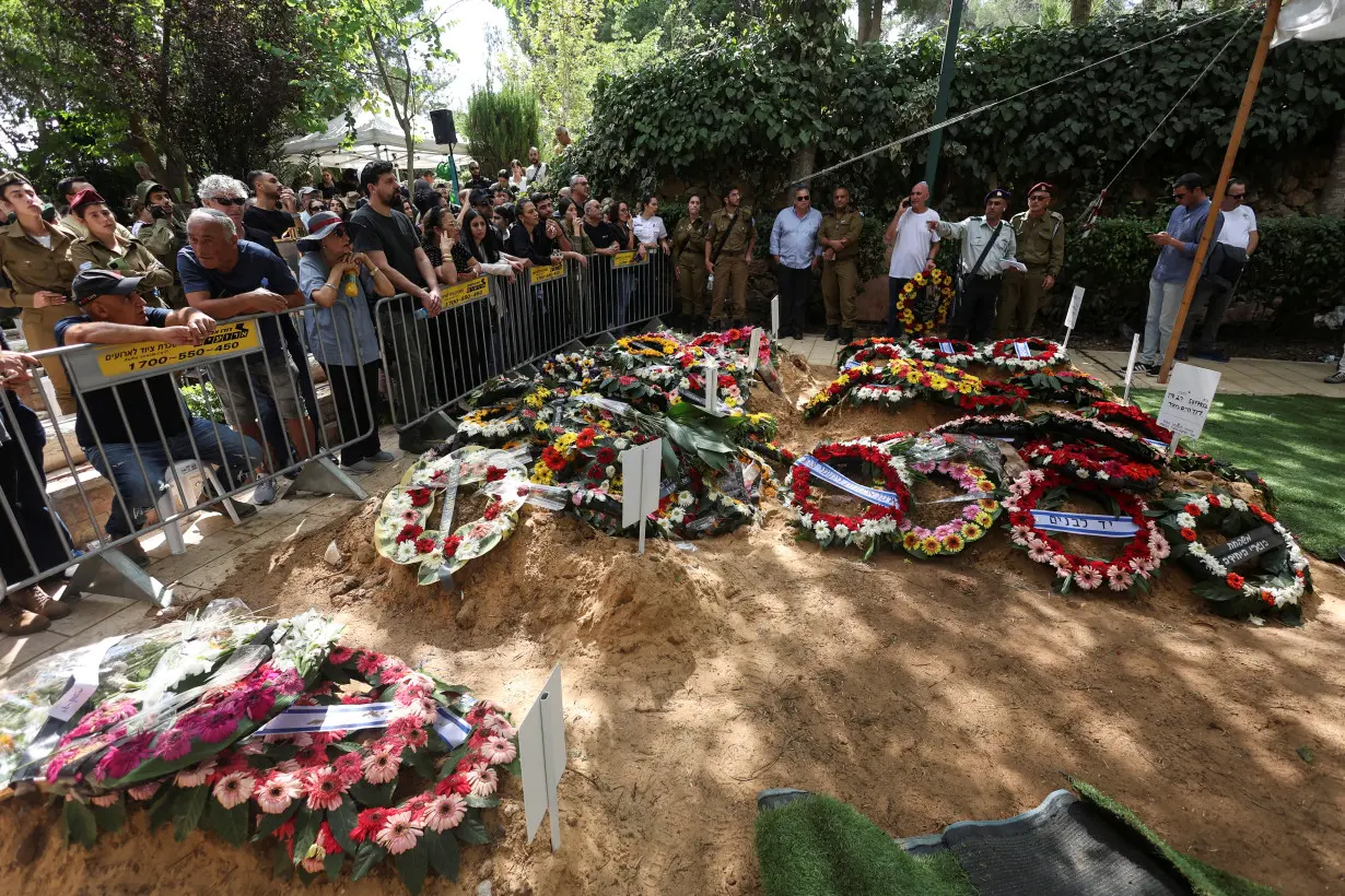 Mourners stand by the fresh graves of Israeli soldiers who were slain in the assault on Israel by Hamas gunmen from the Gaza Strip, in an area of Mount Herzl Military Cemetery prepared in readiness to bury more casualties, in Jerusalem