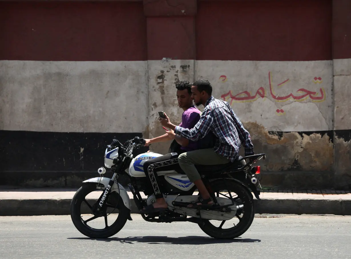 An Egyptian man drives his motorbike in front of a wall painting featuring the Egyptian national flag and text that reads 