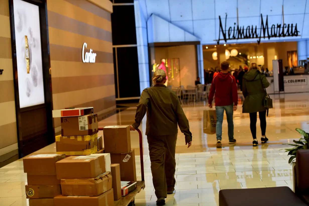 A delivery of boxes is wheeled as shoppers walk towards a Neiman Marcus as holiday shopping accelerates at the King of Prussia Mall