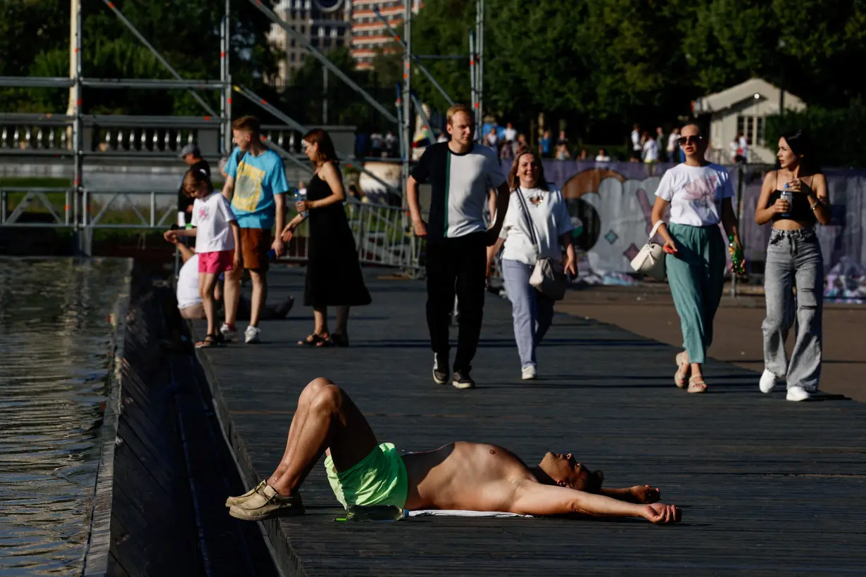 FILE PHOTO: A man lies near a fountain in a park during hot weather in Moscow