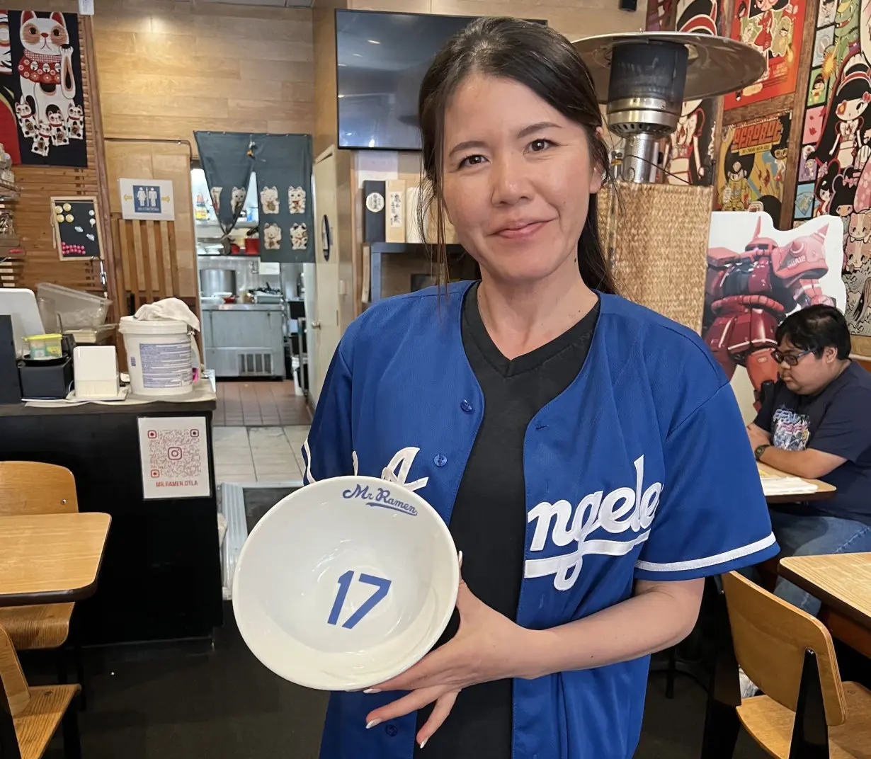 Hiroko Hinata, whose family owns Mr. Ramen, poses for a photo holding a bowl with Ohtani's Dodgers jersey number on it.