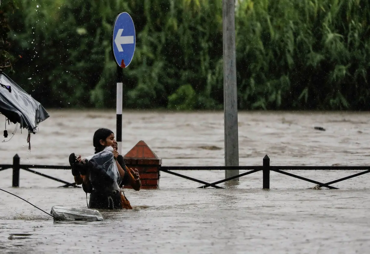 A woman carrying her belongings wades through a flooded road along the bank of overflowing Bagmati River following heavy rains in Kathmandu