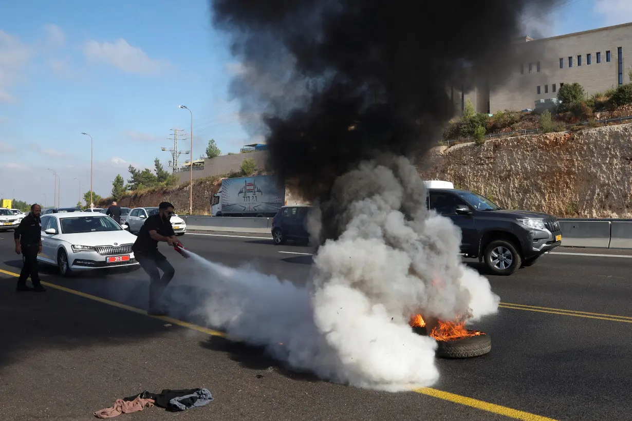 Israeli police extinguish a fire lit by anti-government protestors on a day of protests marking 9 months since the deadly October 7 attack, near Shoresh