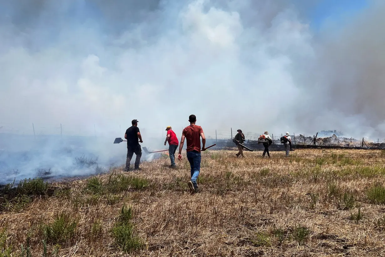 People work to put out fires after Hezbollah launched projectiles at Israel, amid hostilities between Hezbollah and Israeli forces, in the Galilee