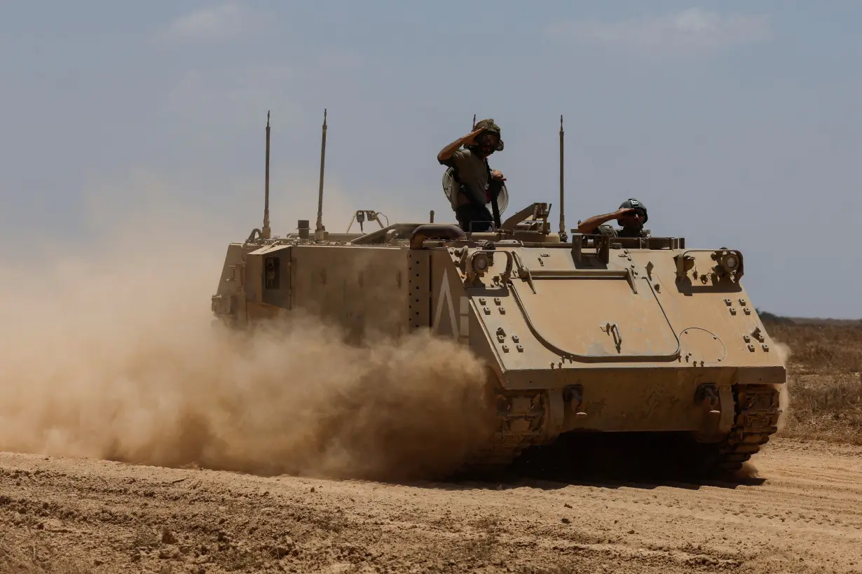 Israeli soldiers salute on a military vehicle as they manoeuvre, near the Israel-Gaza border