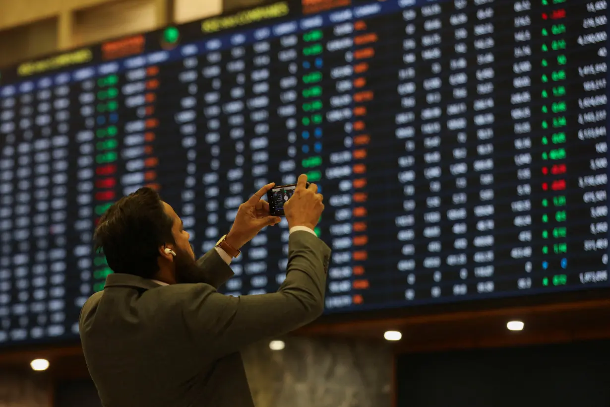 Man takes a photo of the electronic board displaying share prices during a trading session at the Pakistan Stock Exchange, in Karachi