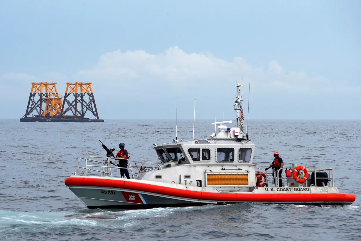 FILE PHOTO: U.S. Coast Guard patrol boat passes a barge carrying jacket supports and platforms for wind turbines in the waters of the Atlantic Ocean off Block Island, Rhode Island