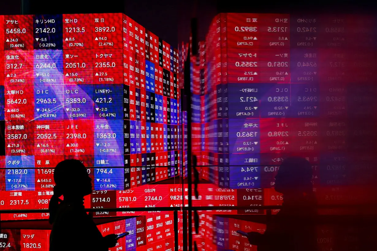 A visitor stands next to an electronic screen displaying Japan's Nikkei stock prices quotation board in Tokyo