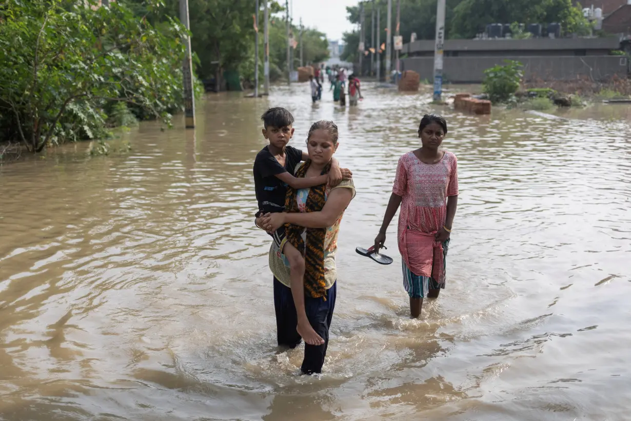 A woman carries her son as she walks through a flooded road after a breach in a canal that supplies water from a nearby state, in New Delhi