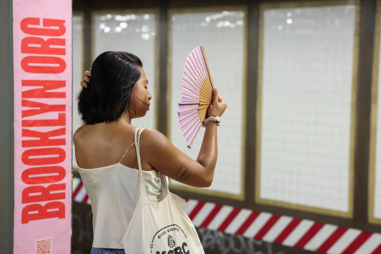 FILE PHOTO: A person uses a fan to cool themselves on a subway platform as high temperatures continue to affect the region in Brooklyn, New York City