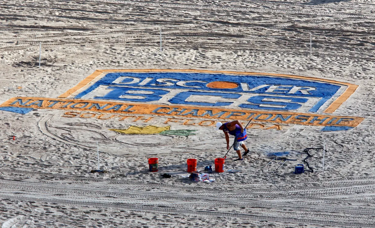 FILE PHOTO: A sand artist paints the sand on Ft. Lauderdale beach with the NCAA college football 2013 Discover BCS National Championship logo in Ft. Lauderdale, Florida