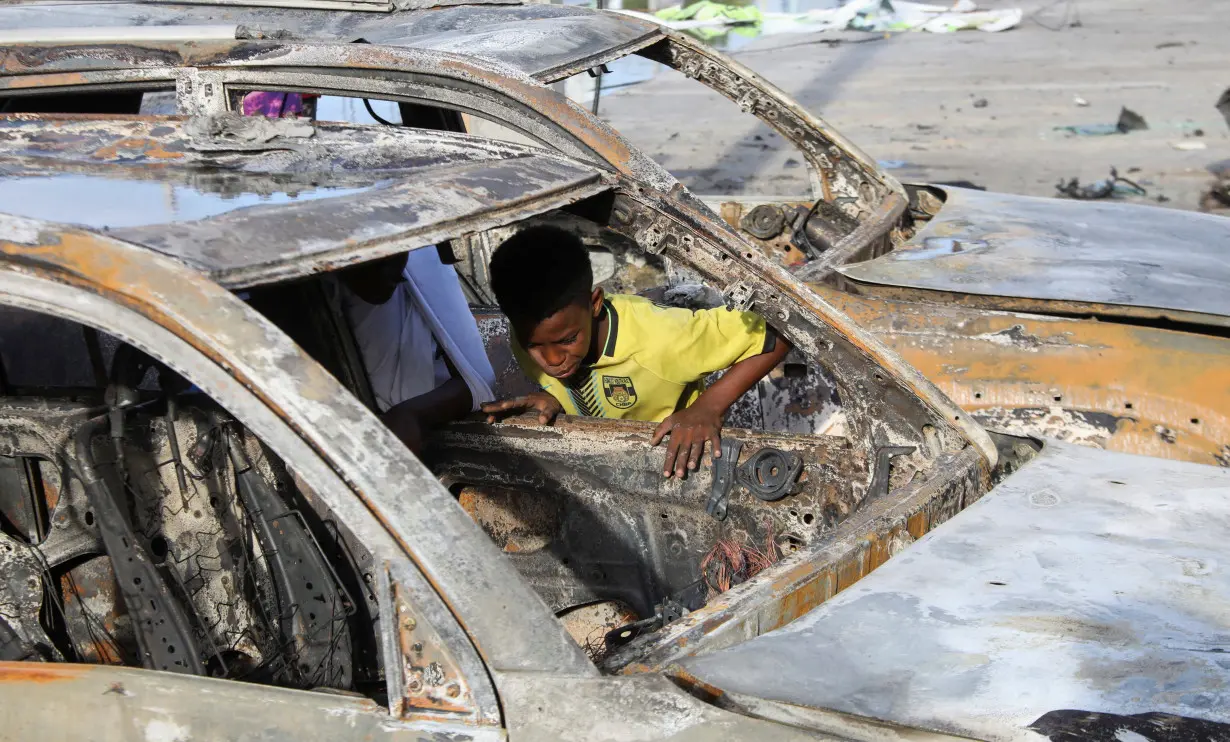 A boy looks through the wreckage of vehicles destroyed at the scene of an explosion outside a restaurant where patrons were watching the final of the Euro 2024 football tournament on TV, in Bondhere district of Mogadishu