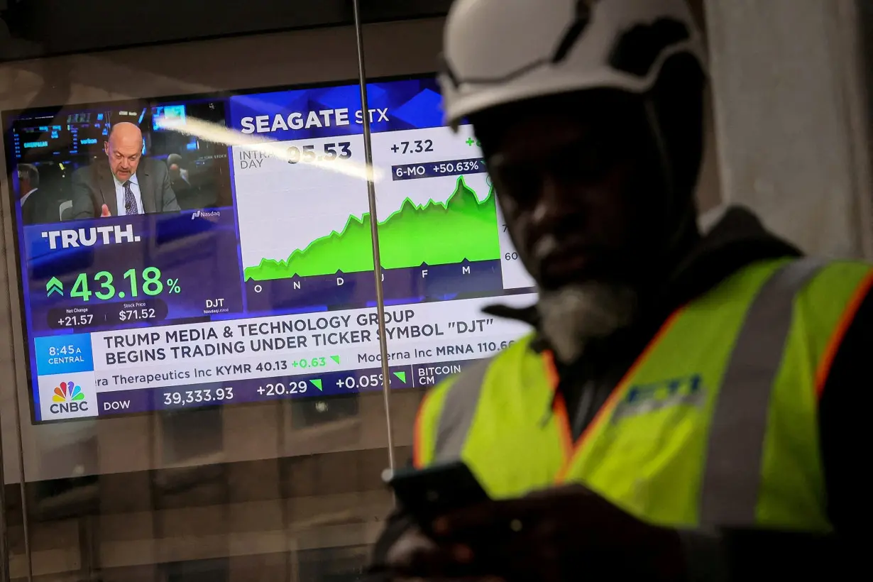 A man looks at this phone as a screen displays trading information about shares of Truth Social and Trump Media & Technology Group in New York