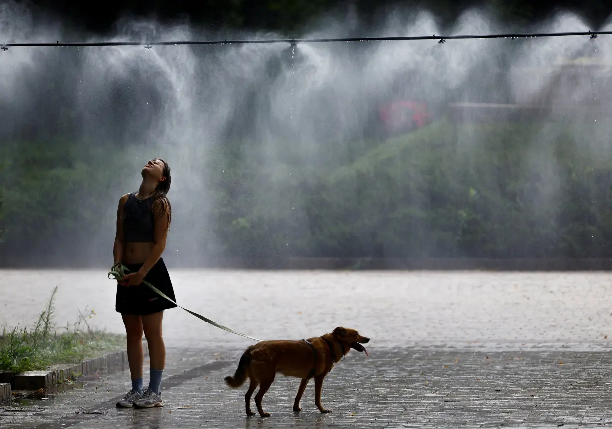 Woman with a dog cools herself under a water sprinkler on an extremely hot summer day in Kyiv