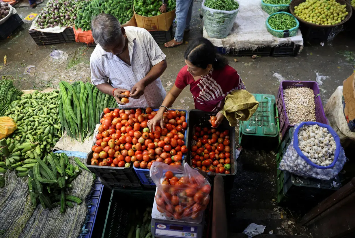 Woman selects tomatoes from a vendor, at a wholesale market in Navi Mumbai