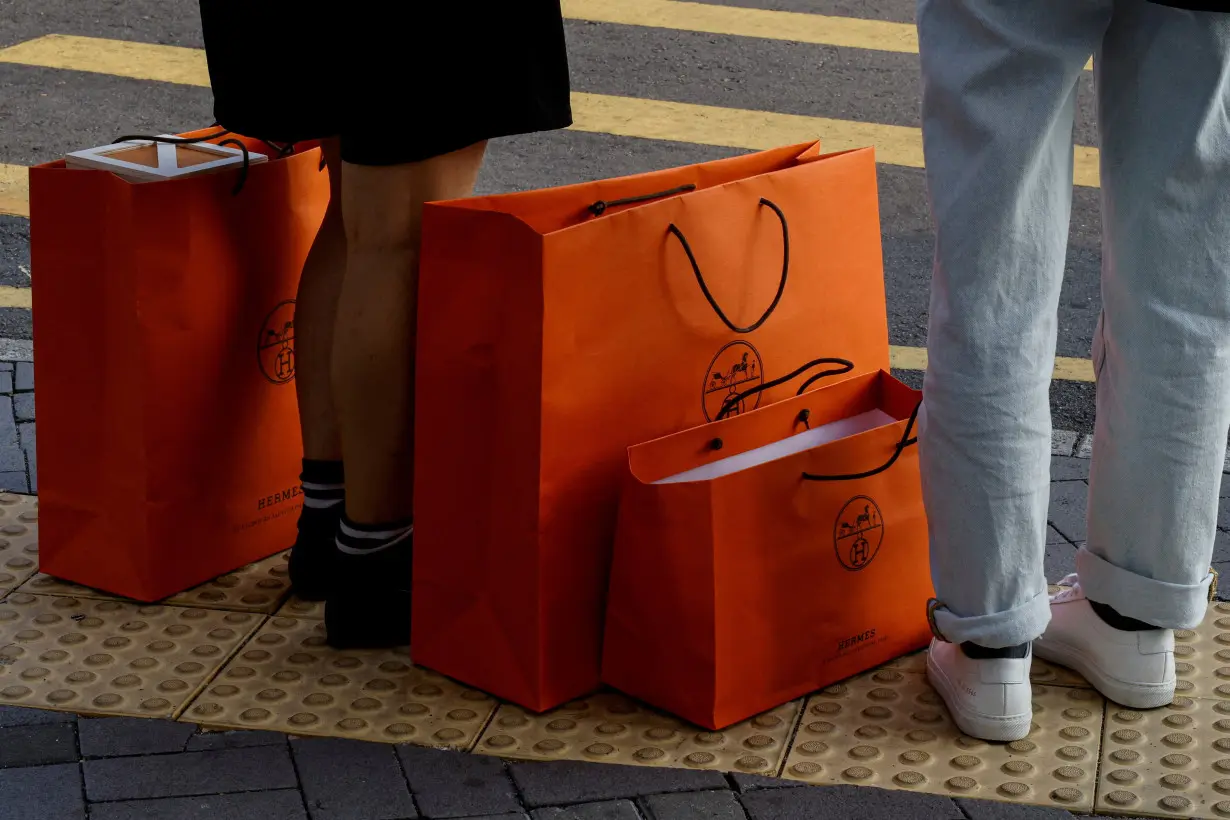 FILE PHOTO: People stand with Hermes shopping bags as they wait at a traffic light in Tsim Sha Tsui, a bustling shopping hotspot, in Hong Kong