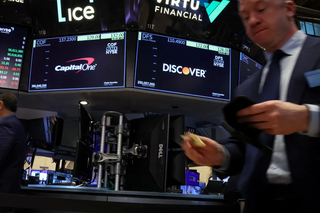 Screens display the logos and trading information for Capital One Financial and Discover Financial as traders work on the floor at the NYSE in New York