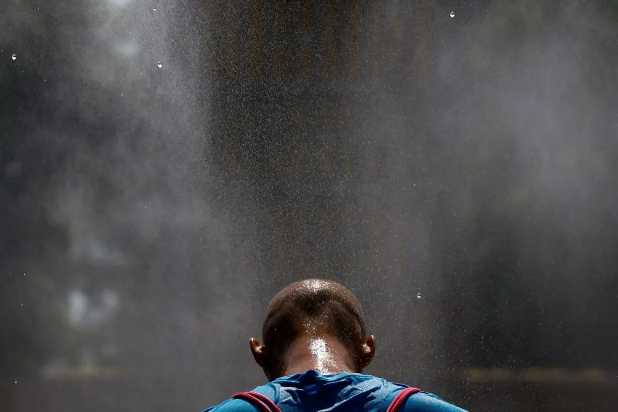 Man cools himself under a water sprinkler on an extremely hot summer day in Kyiv