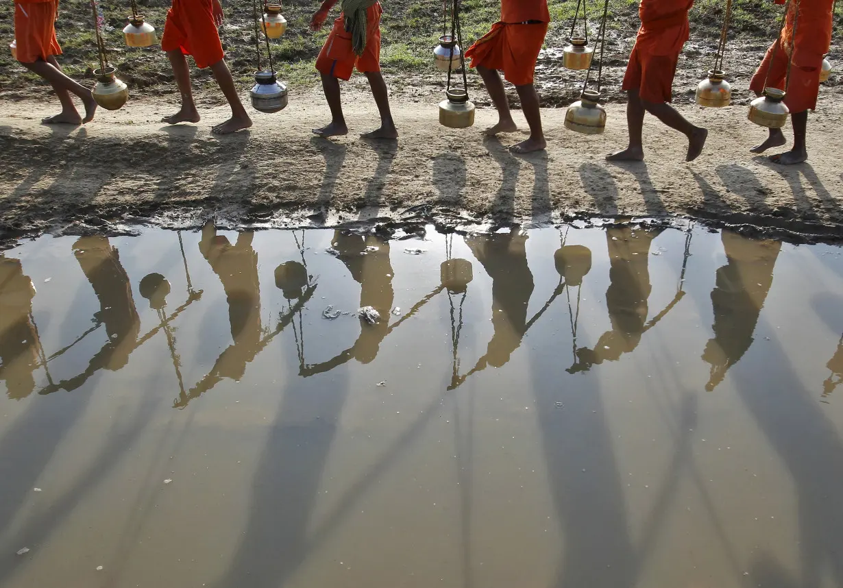 FILE PHOTO: Kanwarias or devotees of Hindu god Shiva carrying pitchers are reflected in a puddle as they walk after filling the pitchers with water from the river Ganges in Allahabad