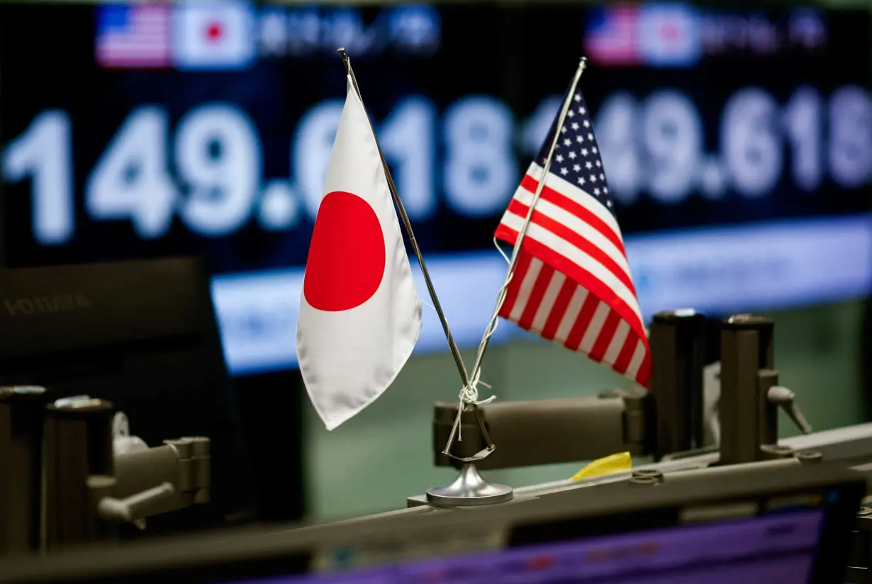 The U.S. and Japanese national flags are displayed next to monitors showing the current Japanese Yen exchange rate against the U.S. dollar, in Tokyo