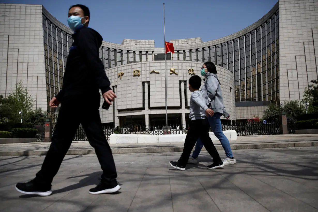 People wearing face masks walk past the headquarters of PBOC, where the Chinese national flag flies at half mast