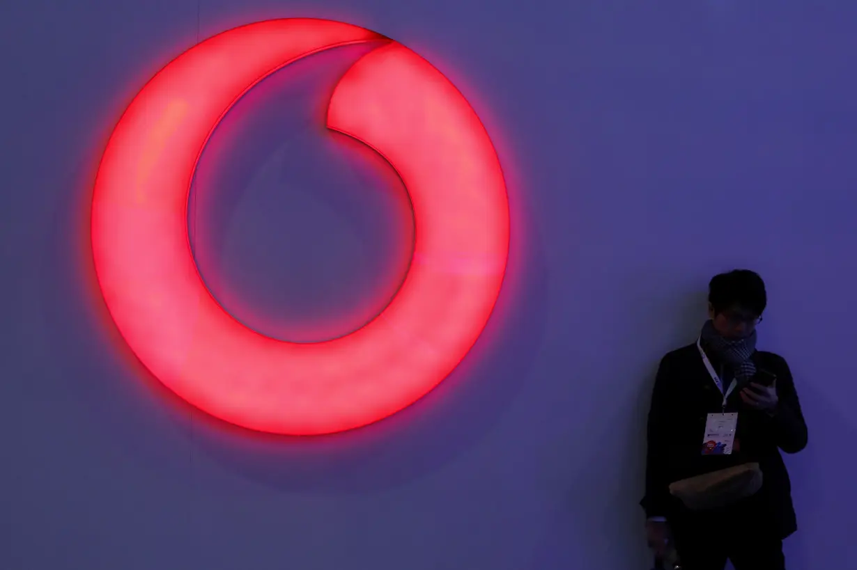 FILE PHOTO: A man checks his mobile phone next to a Vodafone logo at the Mobile World Congress in Barcelona