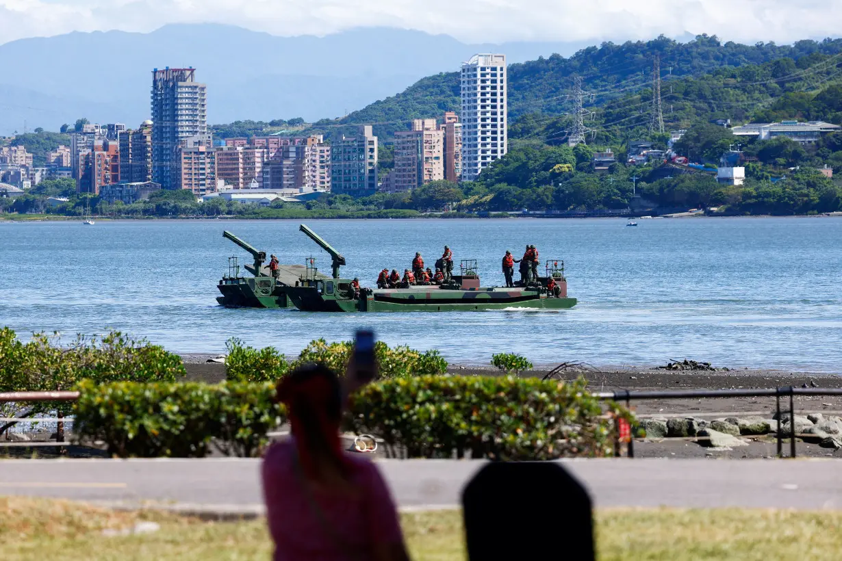 A woman watches as soldiers practice laying mines and nets to stymie the landing of enemy forces at the mouth of a major river in Taipei