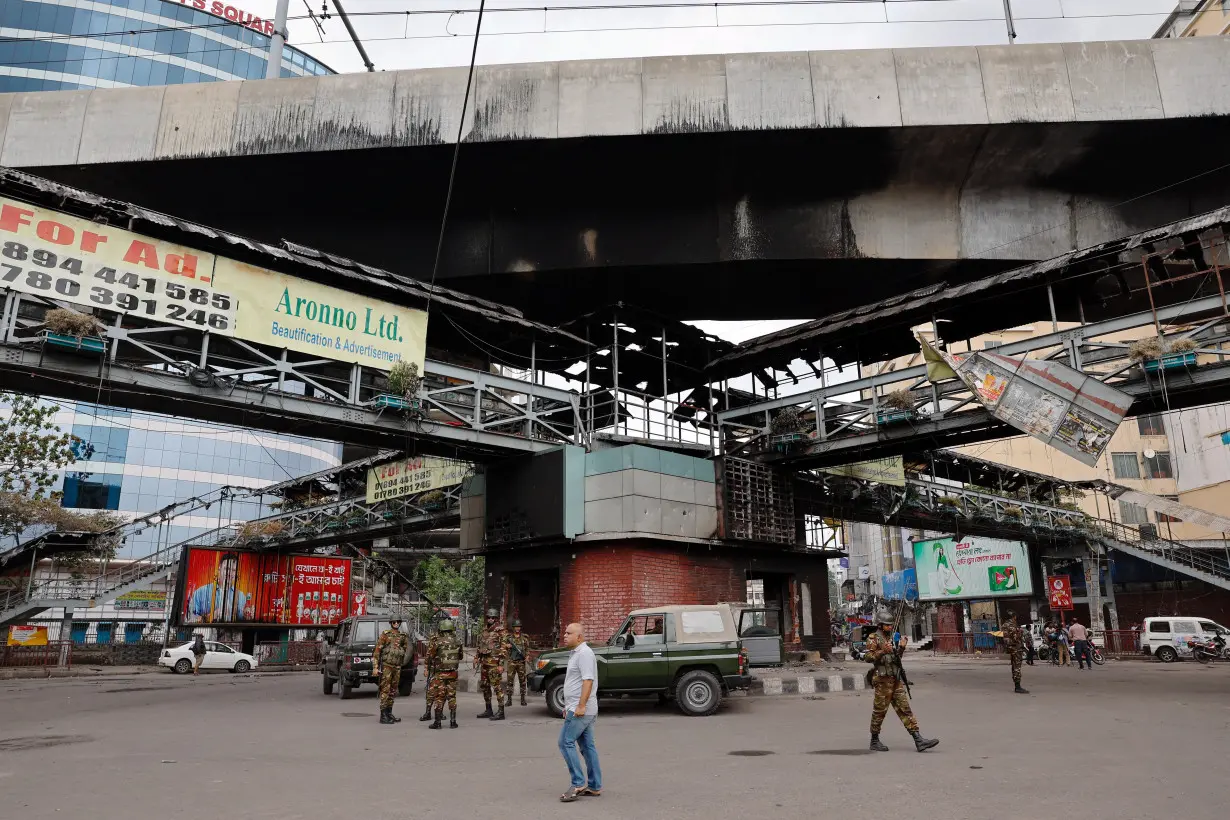 Army soldiers stand guard under a footbridge that was set on fire by a mob during clashes after violence erupted following protests by students against government job quotas, in Dhaka