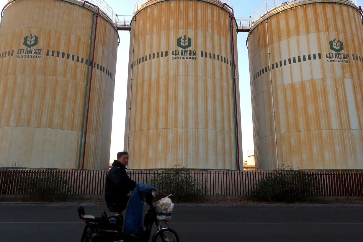 FILE PHOTO: Man cycles past storage facilities of China's state grain stockpiler Sinograin near Tianjin port